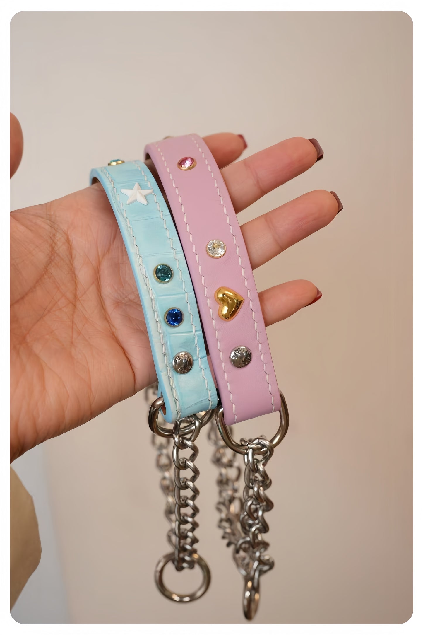 Two colorful dog collars with charms held by a hand against a neutral background