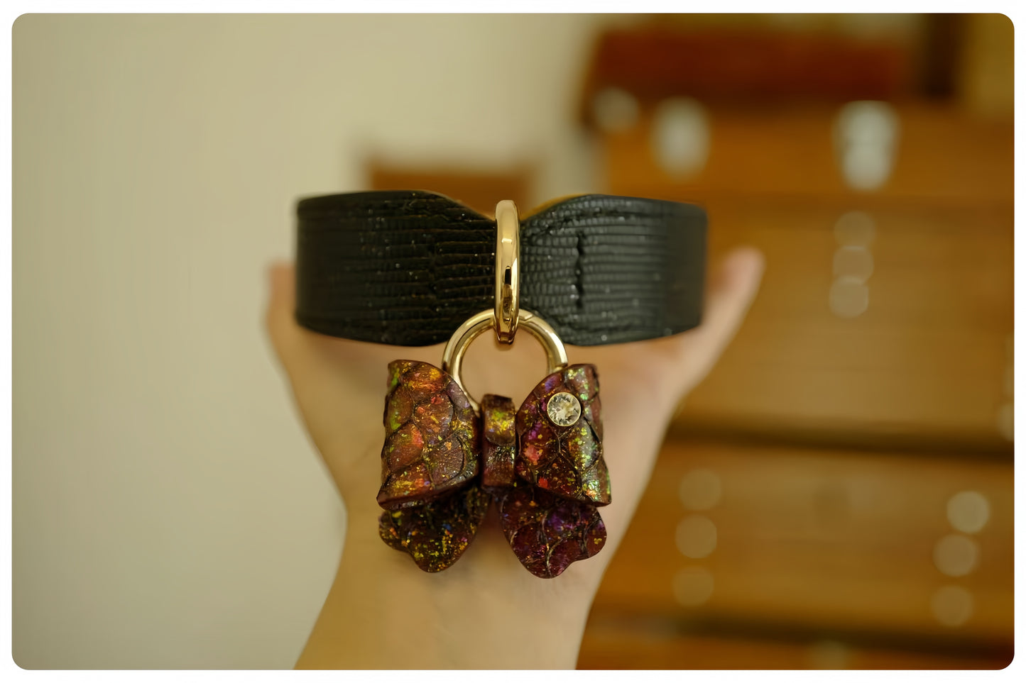 Black dog collar with a decorative bow charm held by a hand against a blurred background