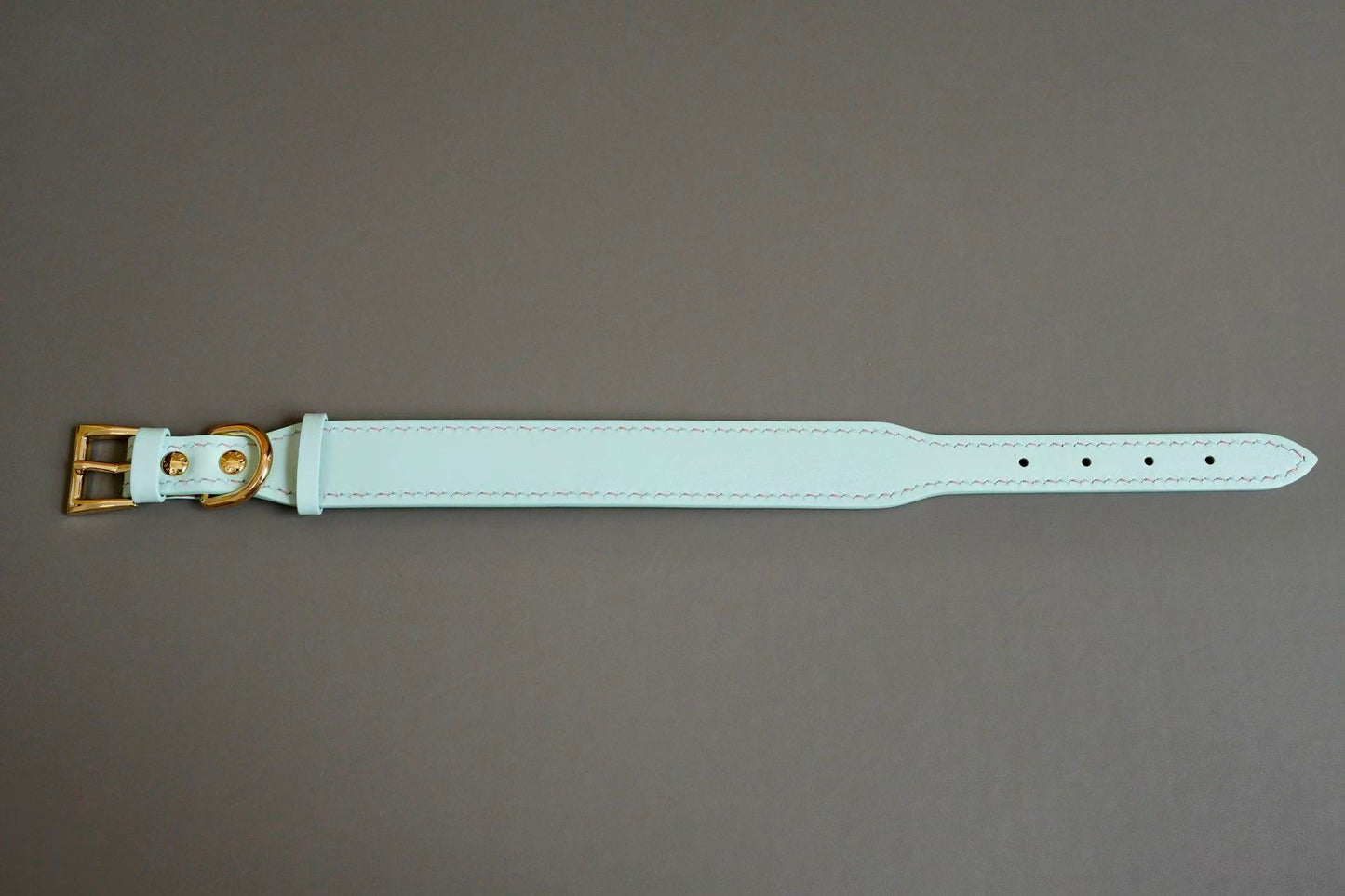 Light blue leather belt with a gold buckle on a gray background