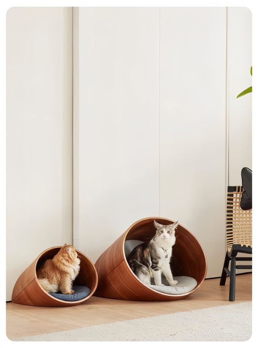 Two cats in wooden cat houses against a white wall.