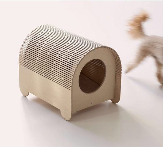 Cardboard cat house on a white surface with a blurred cat in the background